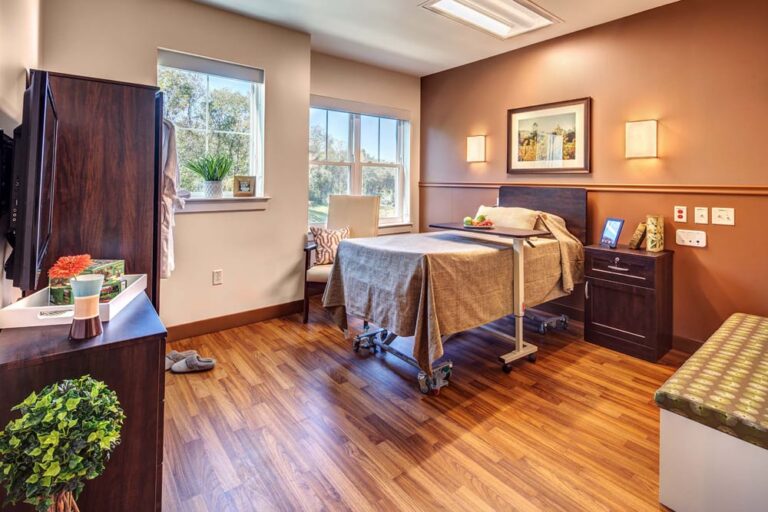 Senior living patient room at Village Point with framed nature photography above the bed, warm brown accent wall, and wood flooring